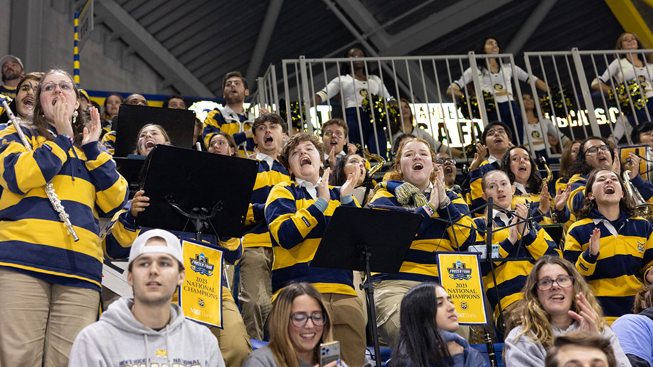 Members of Quinnipiac's pep band smile and cheer in the stands
