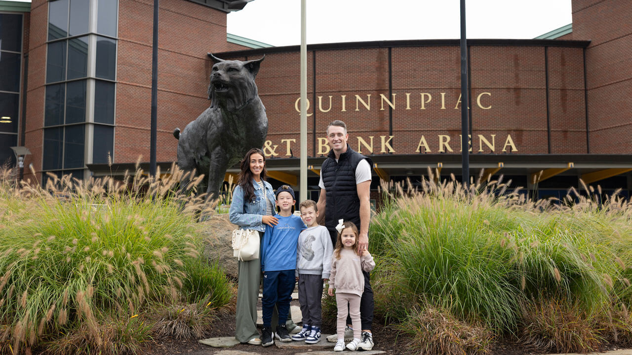 Alumni and their children take a photo in front of the M&T Bank Arena