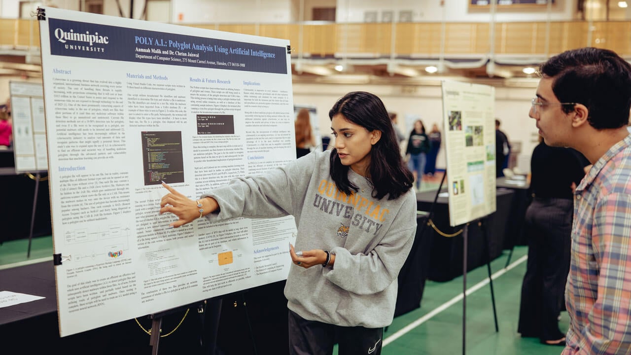 A student points to her academic poster as she presents her research to an Exploratorium attendee.