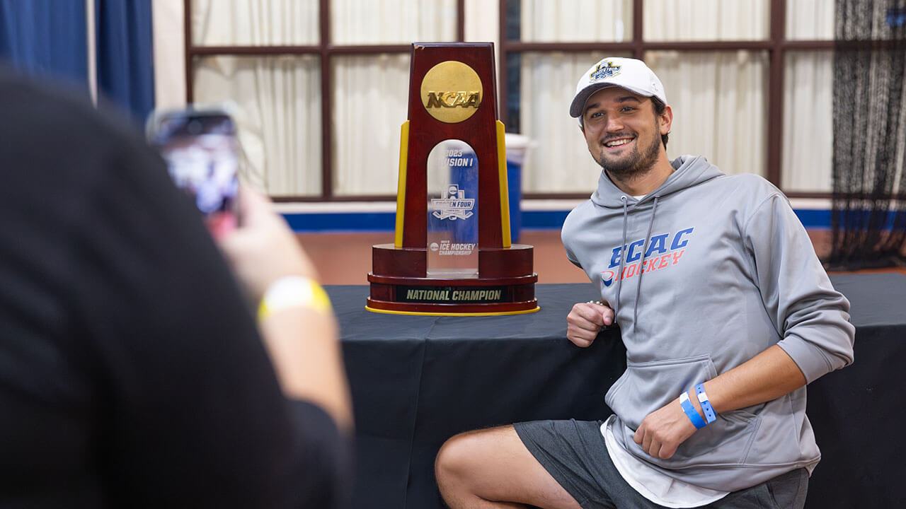 Student smiles while crouching in front of the NCAA National Championship trophy