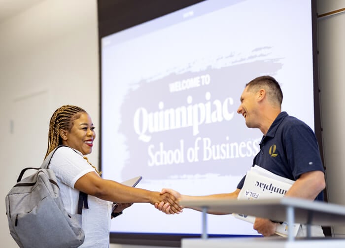 A School of Business professor smiles, shaking hands with a student.