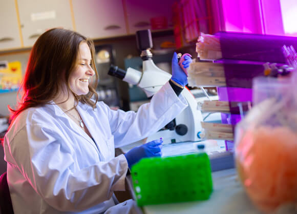 Female student in a lab smiling while using lab equipment
