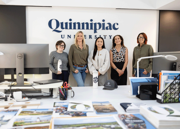 Five individuals stand in front of a Quinnipiac University sign smiling