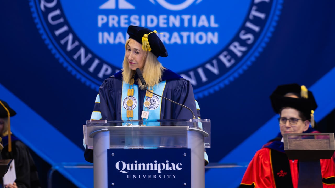 Marie Hardin wearing her Inauguration regalia smiles from behind the podium