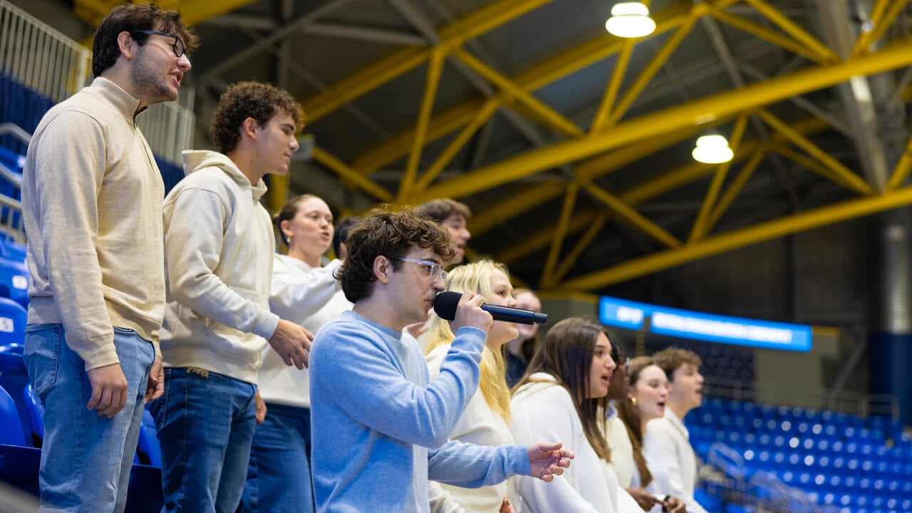 Members of The Legends a cappella group wear white and sing in the stands