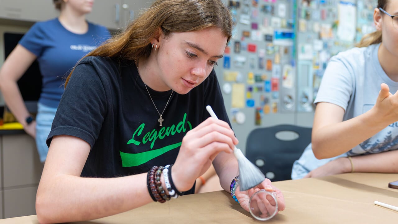 A high school student uses a soft brush to dust a clear glass for fingerprints during a forensic science lab at Quinnipiac University.