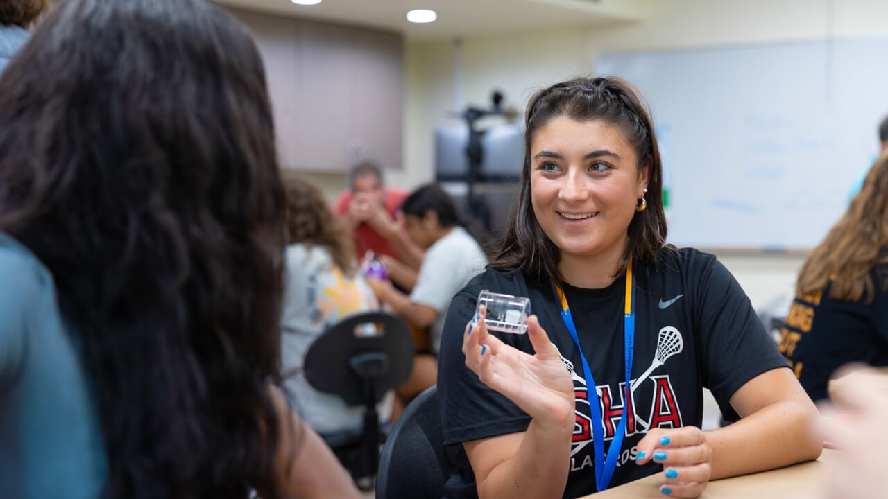 A high school student smiles while showing a small plastic container holding a fingerprint sample during a forensic science activity at Quinnipiac University.