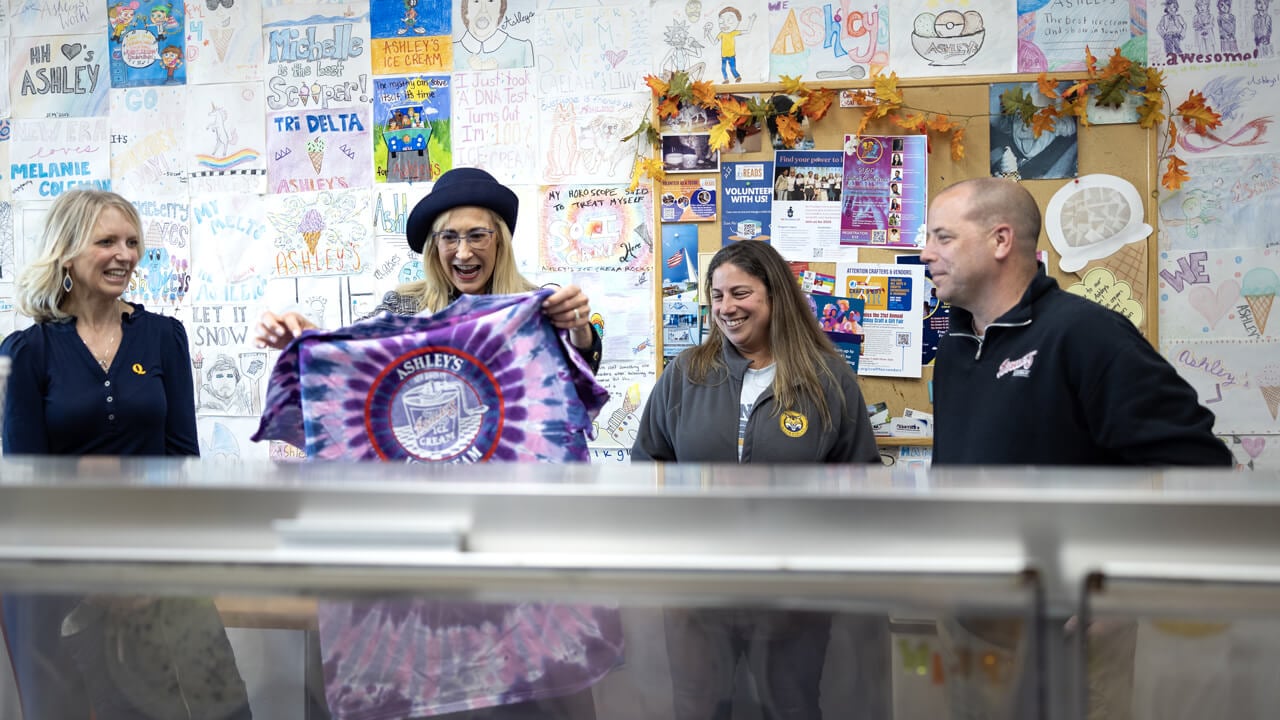 Marie Hardin holds up a bright tie dye Ashley's Ice Cream tee shirt while staff look on
