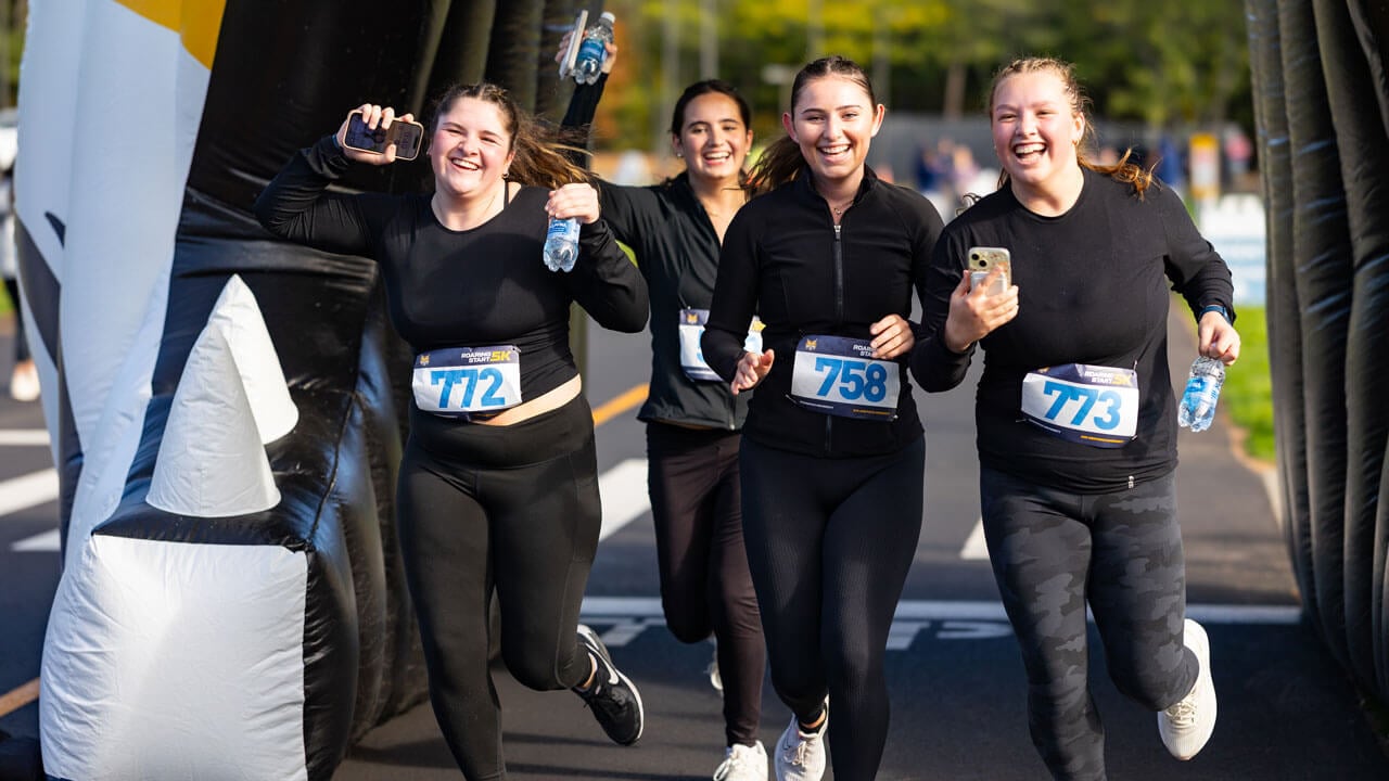 Four runners race through the bobcat head with excited faces as they finish the race