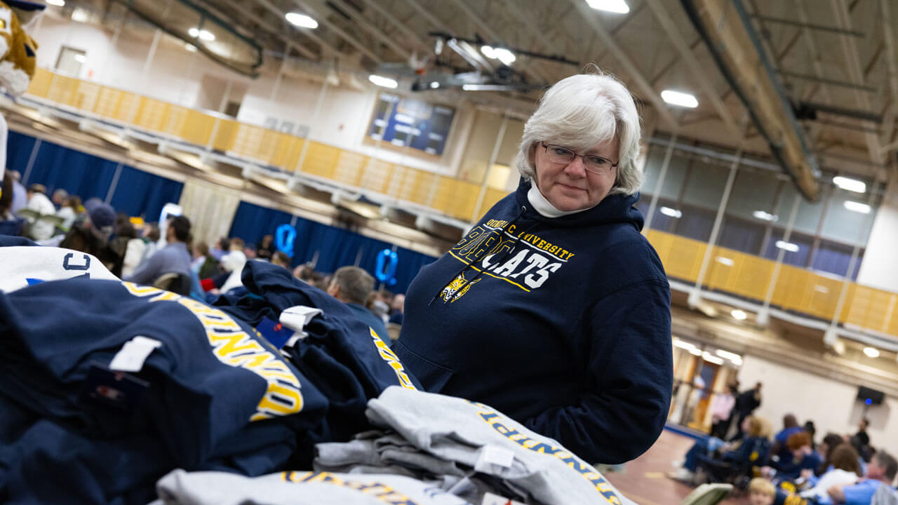 Woman looks down at Quinnipiac sweatshirts laid out on a table