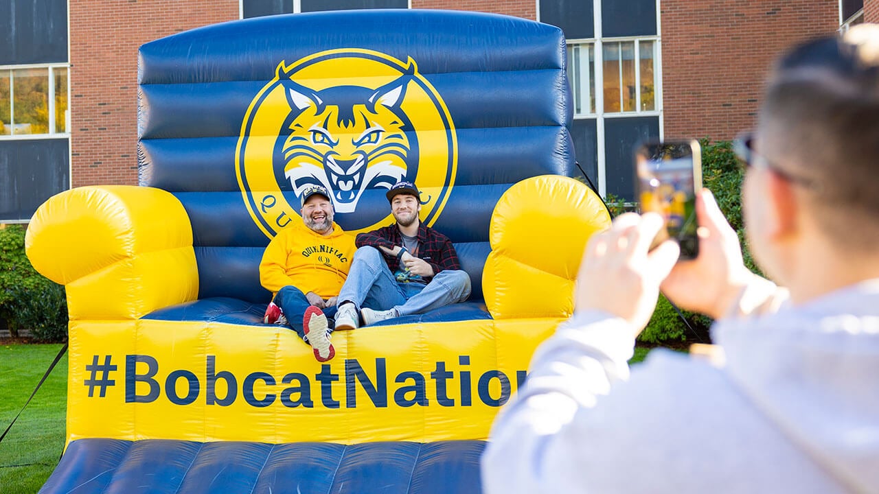 Bobcats smile for a photo on a giant Quinnipiac chair.