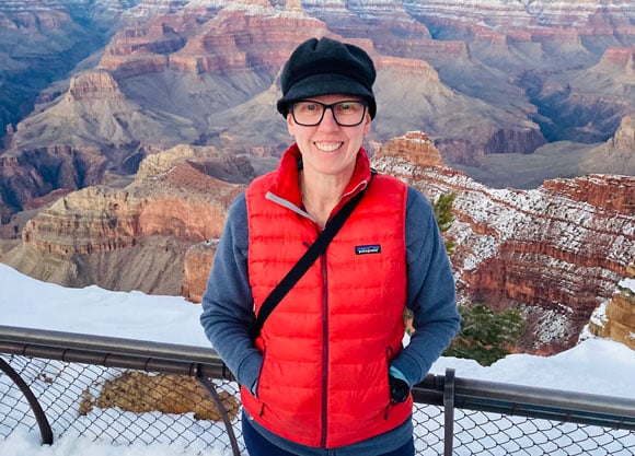 Cheryl Sturgis stands in front of the Grand Canyon wearing a hat and vest.