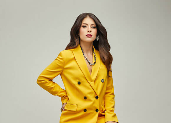 Savannah Giammarco sits in a bright yellow pantsuit with a serious expression on her face.