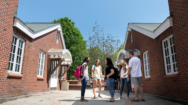 Five students stand together by the Quinnipiac Commons Residence Hall at the Mount Carmel Campus