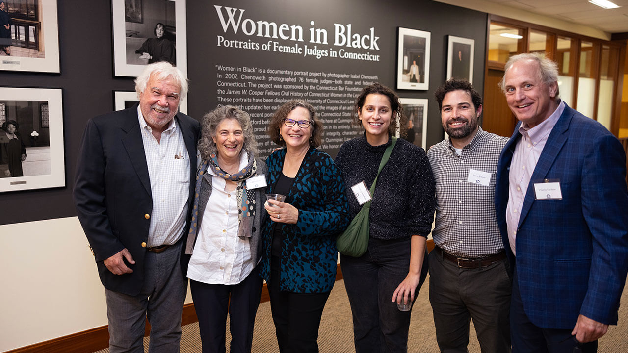 Six individuals take a photo in front of the new "Women in Black" gallery exhibit in the School of Law