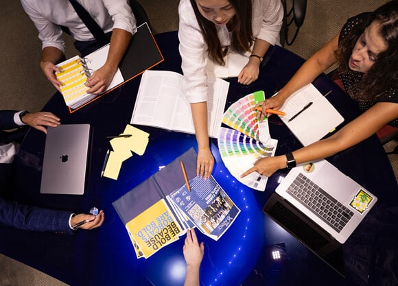 Faculty and students collaborate around a table in The Agency