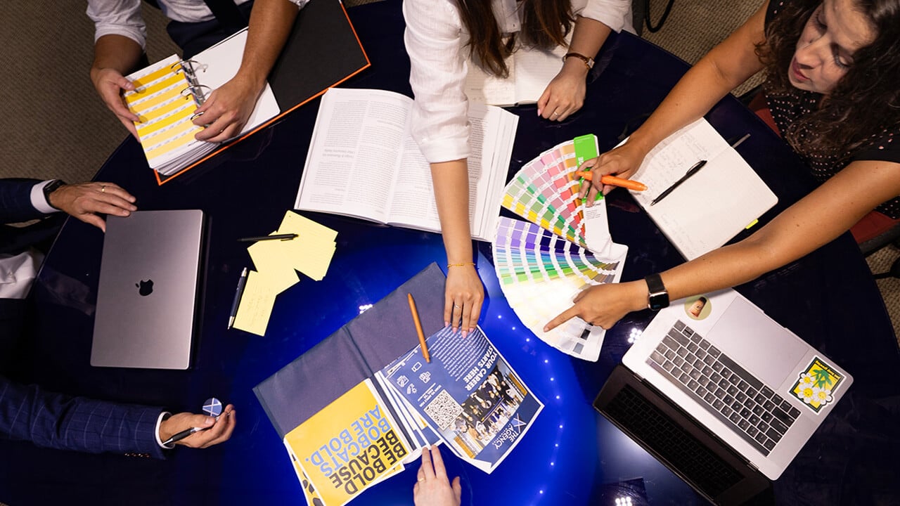 Faculty and students collaborate around a table in The Agency