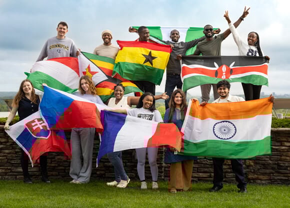 A group of international students smile and wave flags from their home countries on the York Hill Campus