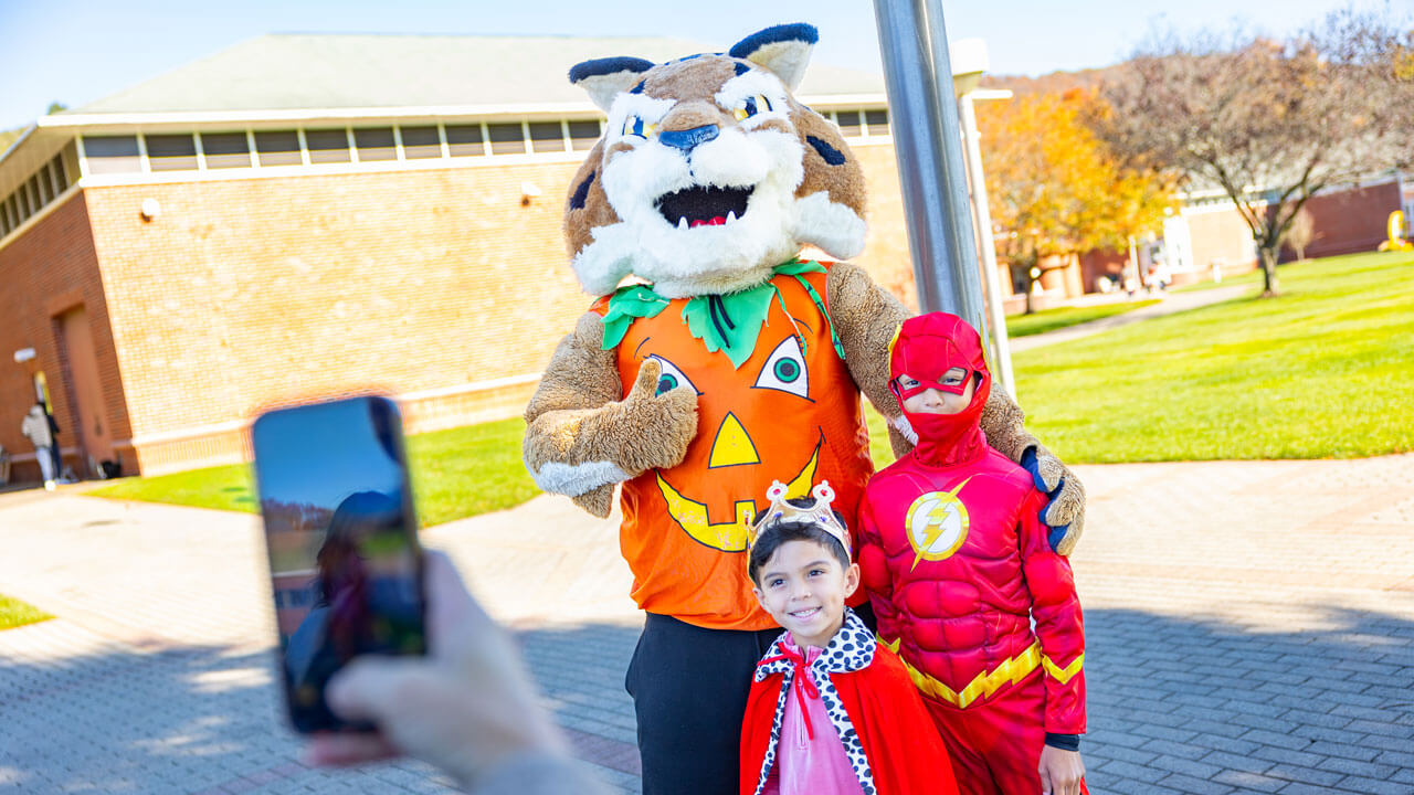 Boomer holds a thumbs up while posing with children dressed in halloween costumes