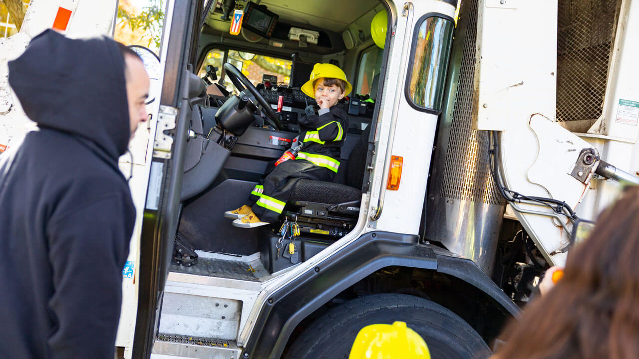 Child dressed in a fire fighter costume sits in the driver seat of a fire truck