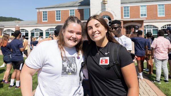 Two international students pose for a photo while several students walk behind them