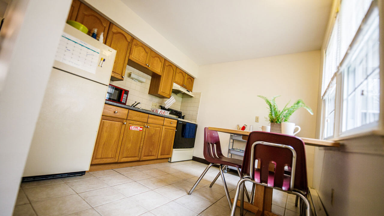 A kitchen with a fridge, table, and 4 dining chairs in Whitney Village apartment complex