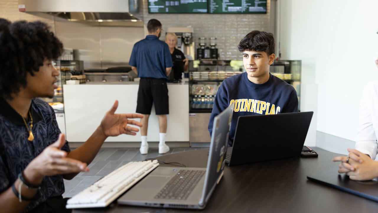 2 students talking at a table with their laptops at the School of Business Cafe