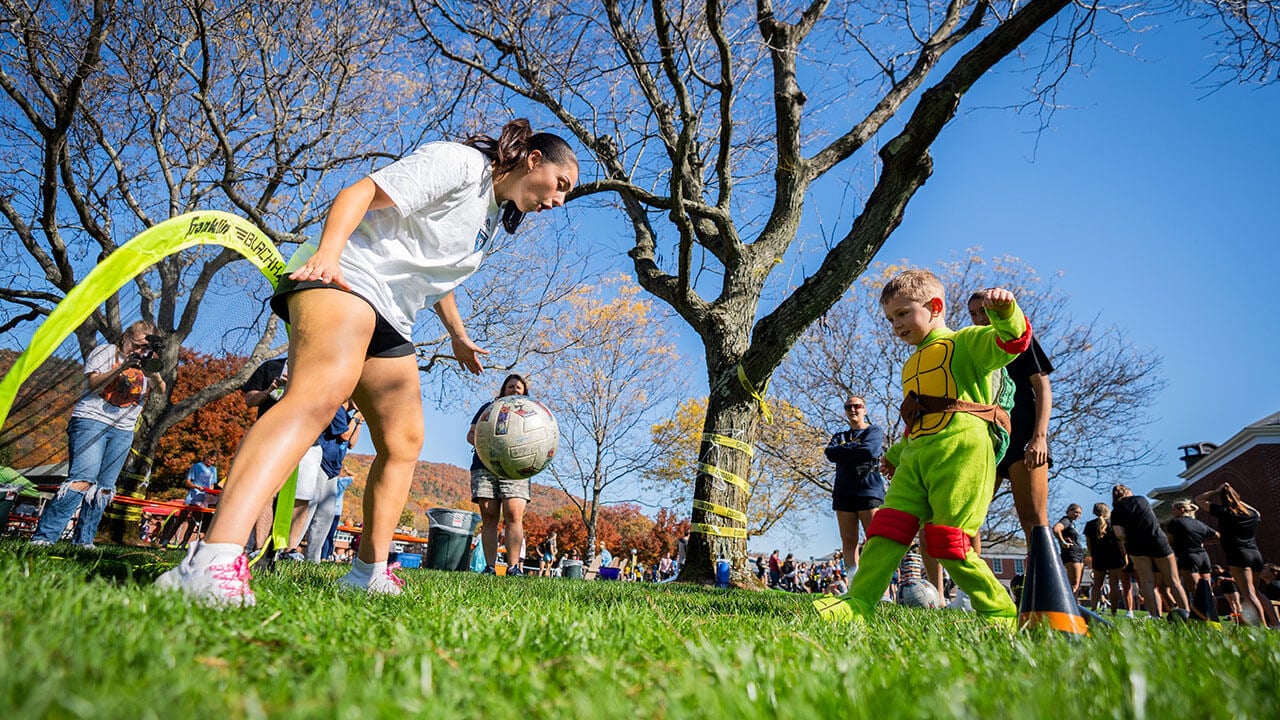 Kids in costumes playing soccer with Quinnipiac athletes
