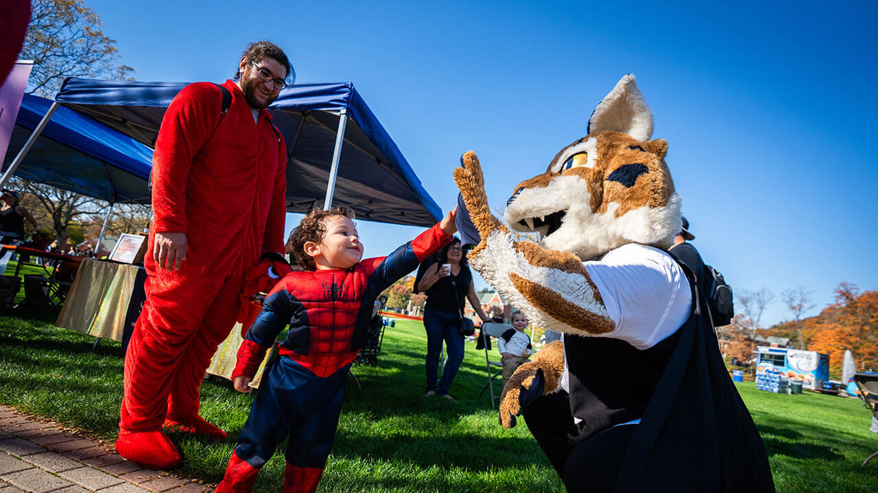 Little kid dressed up as spider man high-fiving Boomer the Bobcat