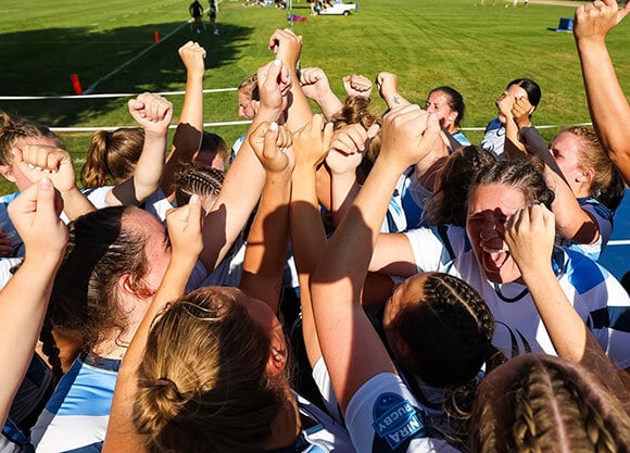 The women's rugby team celebrates on the field.