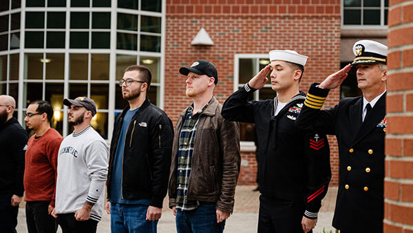 Veterans stand at attention and saluting on the Mount Carmel Campus quad.