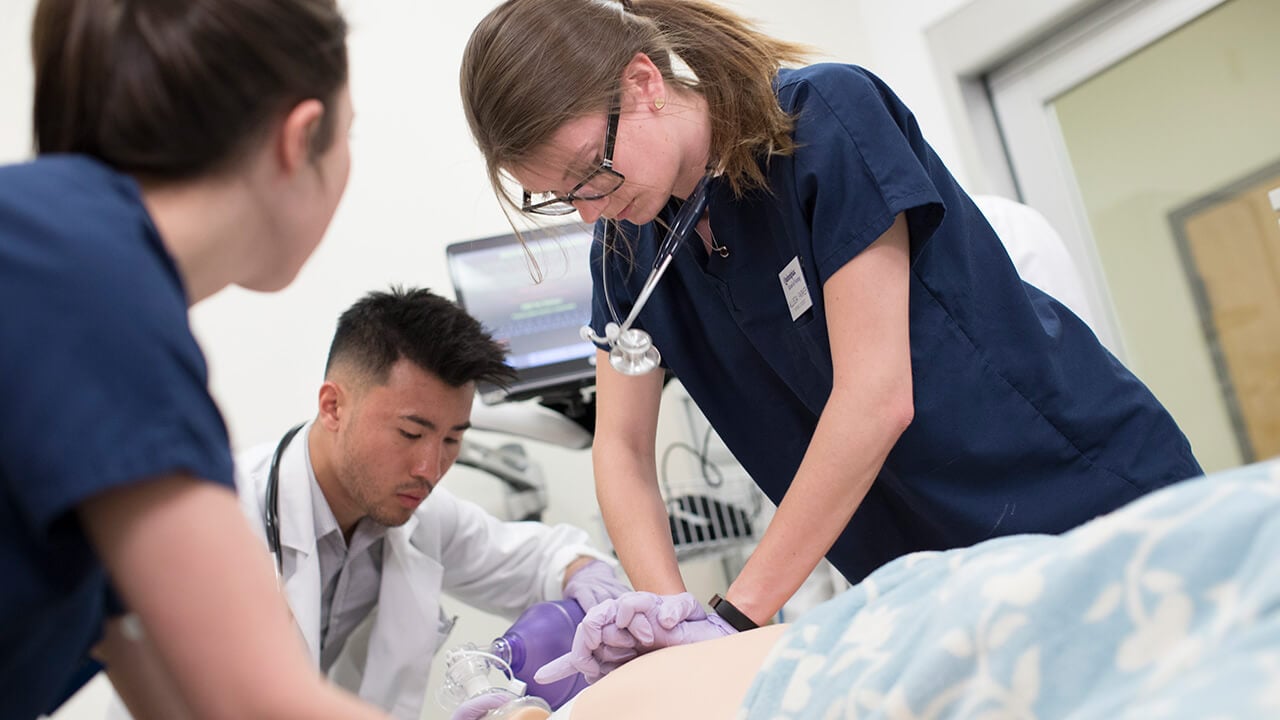 A physician assistant student and nursing student collaborate with a PA faculty member to administer treatment and perform CPR on a mannequin in the simulation suite on the North Haven Campus.