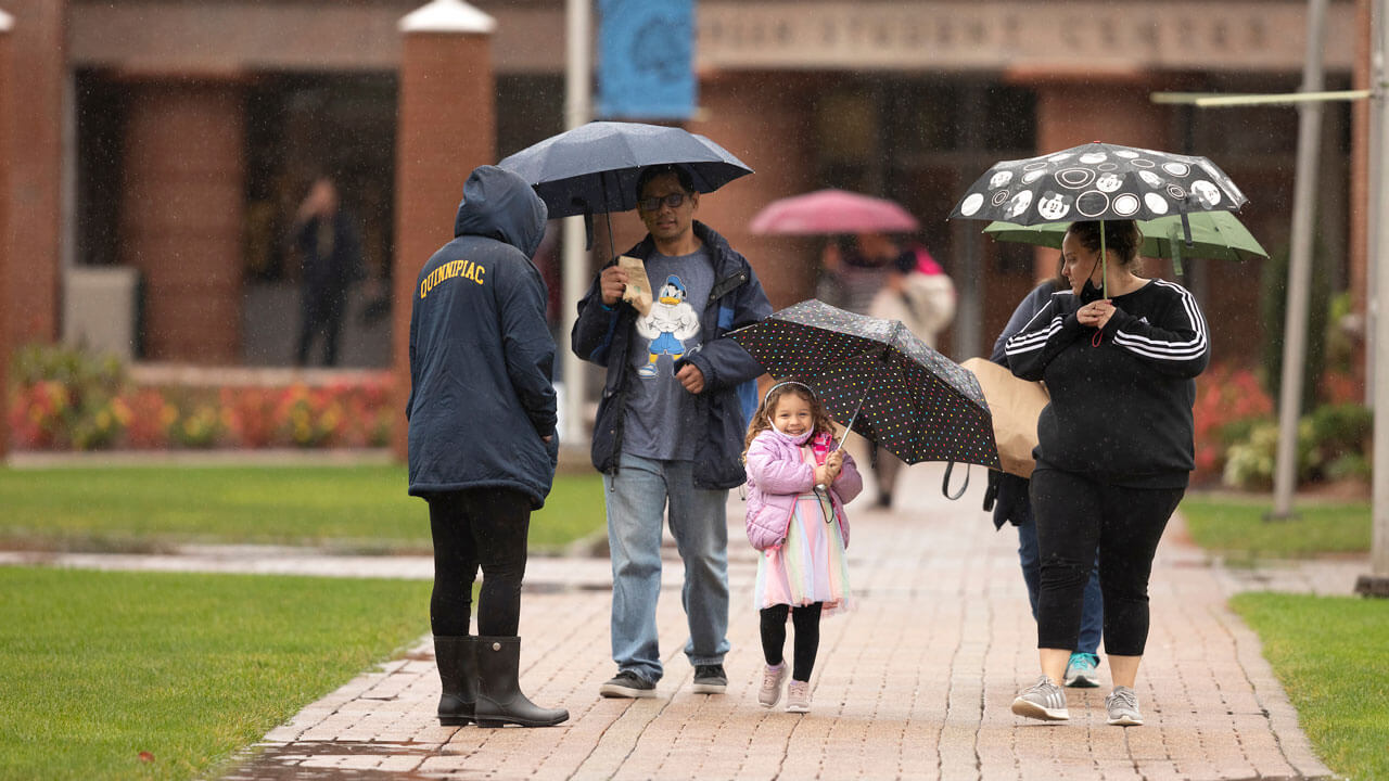 Little girl and parents walking on quad while holding umbrellas in the rain during bobcat weekend