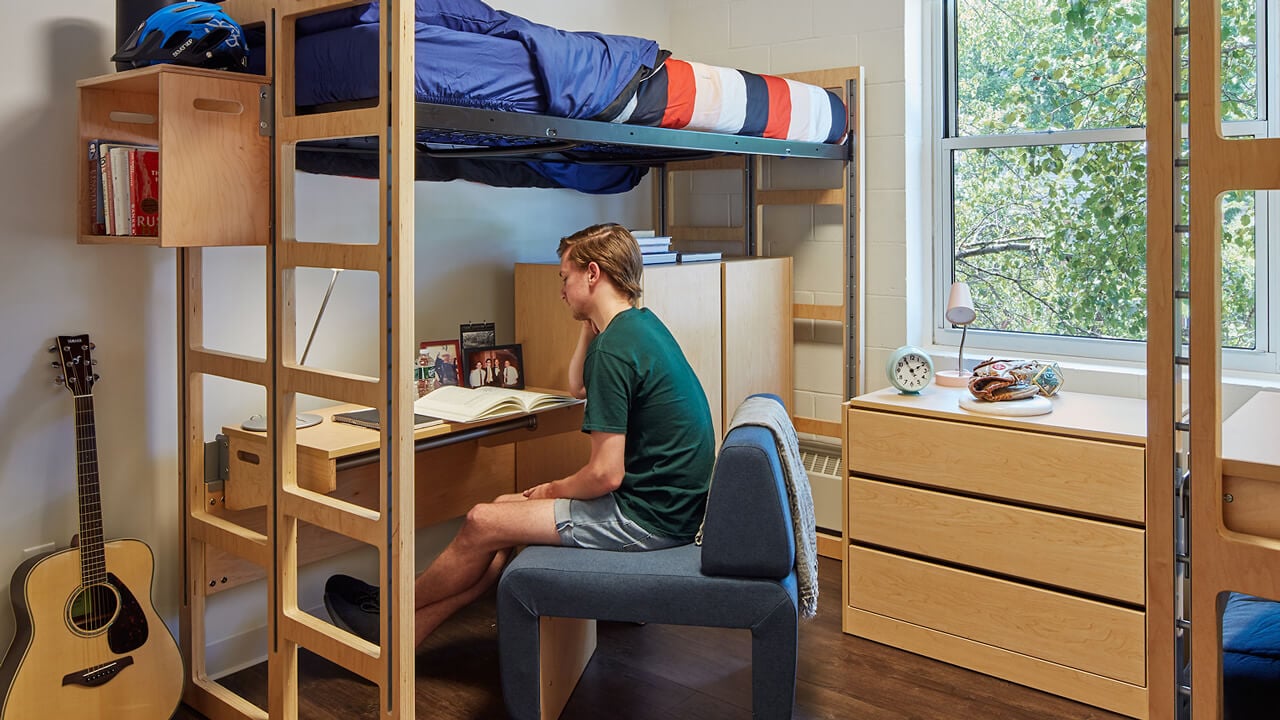 A student studies at his desk under his lofted bed