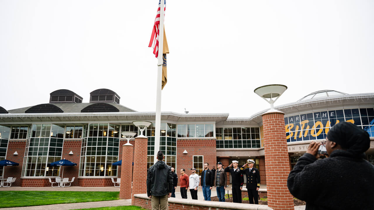 Jason Burke and student veterans salute the American flag in front of the Quinnipiac student center