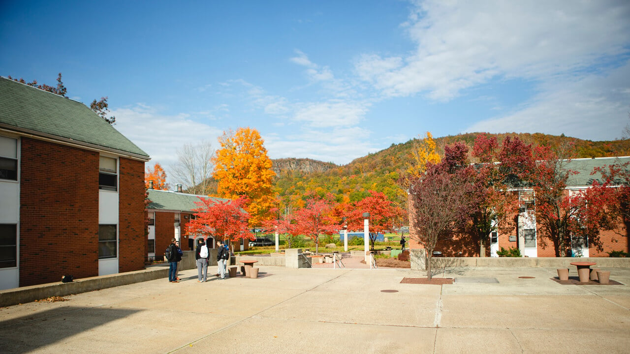Students talk in a courtyard outside residence halls with Sleeping Giant State Park in the background on a fall day