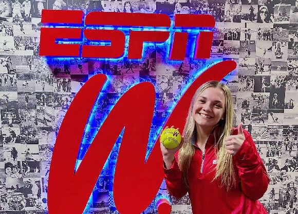 Lo Yarnall holding a softball and smiling in front of an ESPN W sign