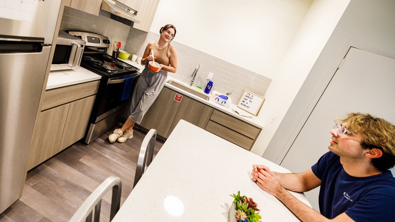 Two students talk and cook in their fully furnished apartment kitchen