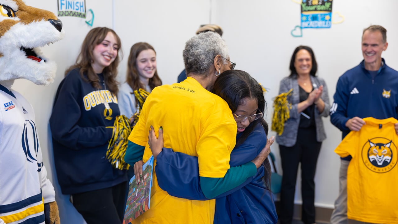 A new student hugs her grandma while people around them clap