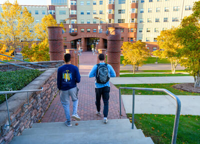 Two upper-class students walk toward the Crescent residence hall on a sunny fall day