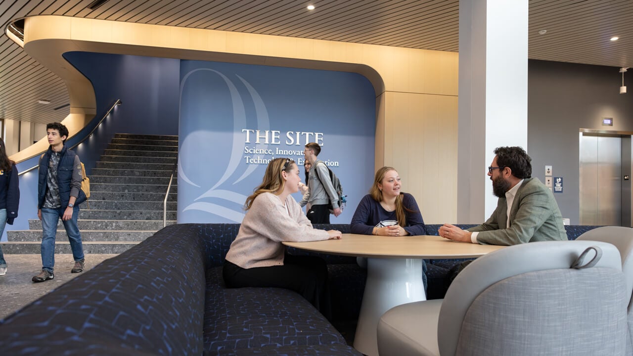 Two students speak with a dean in the lobby of The SITE as other students walk by