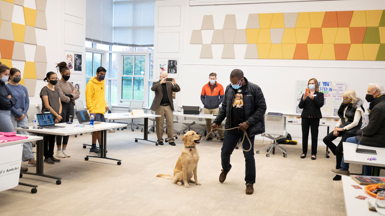An entrepreneurship student leads a dog on a leash while several people look on during a showcase