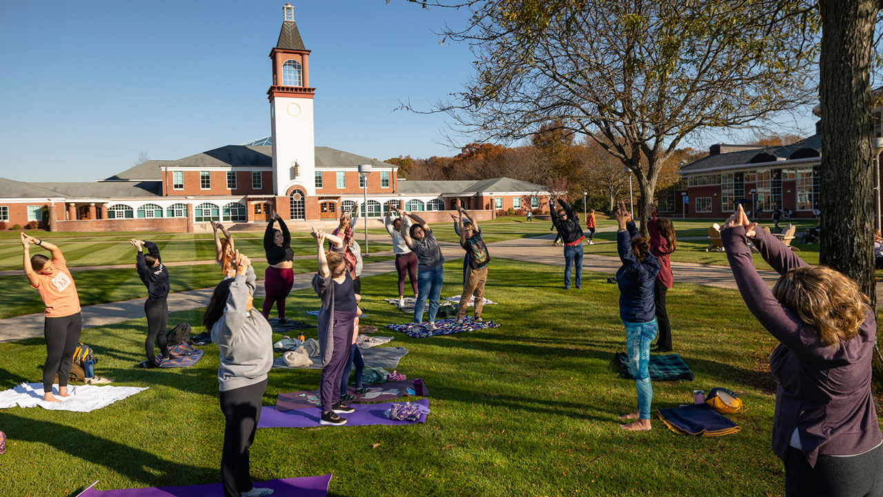 Dozens of women stretch on yoga mats on the quad lawn
