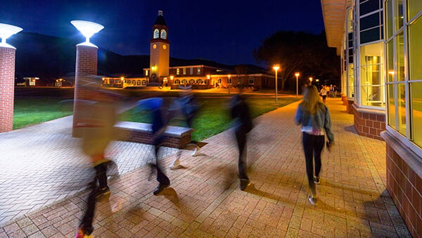 Students walk across the Quad at night.