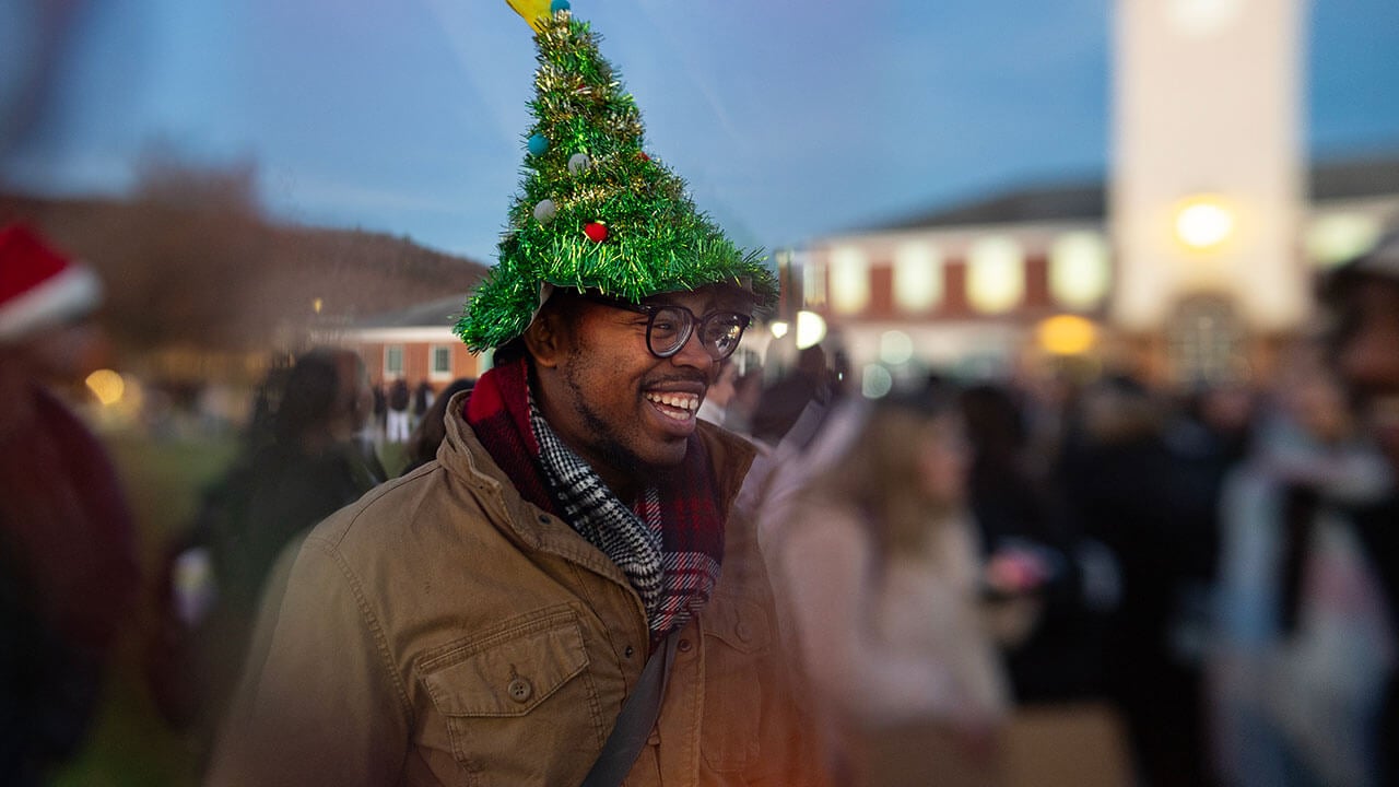 Student wears holiday hat and smiles surrounded by peers