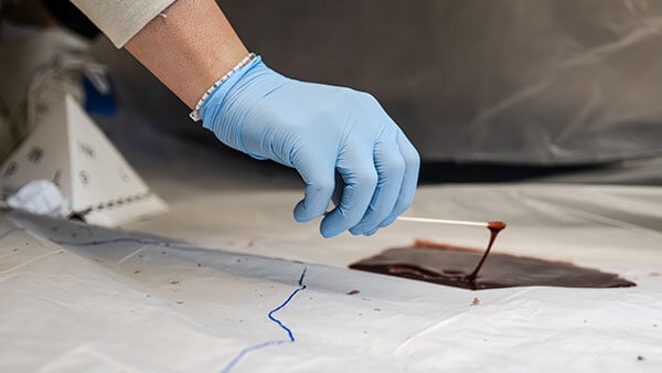 Gloved hand tests a crime scene at a summer camp for high school students