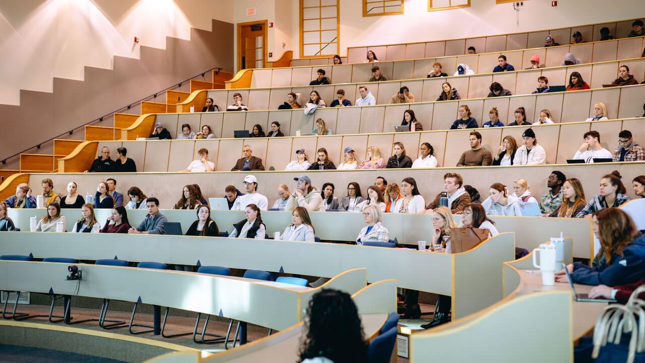 A wide photo of students and panel attendees sitting in a lecture hall.
