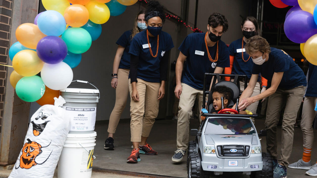 Physical therapy students cheer as a small child drives his modified car