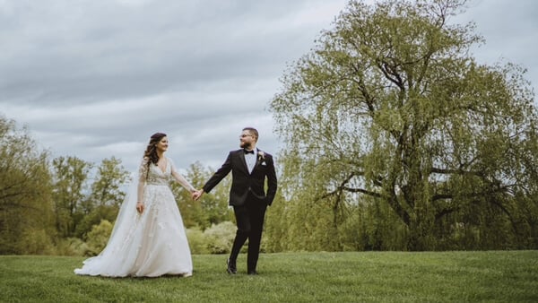 Andy Thane and Amy (Brenner) Thane hold hands and walk in front of a row of trees on their wedding day
