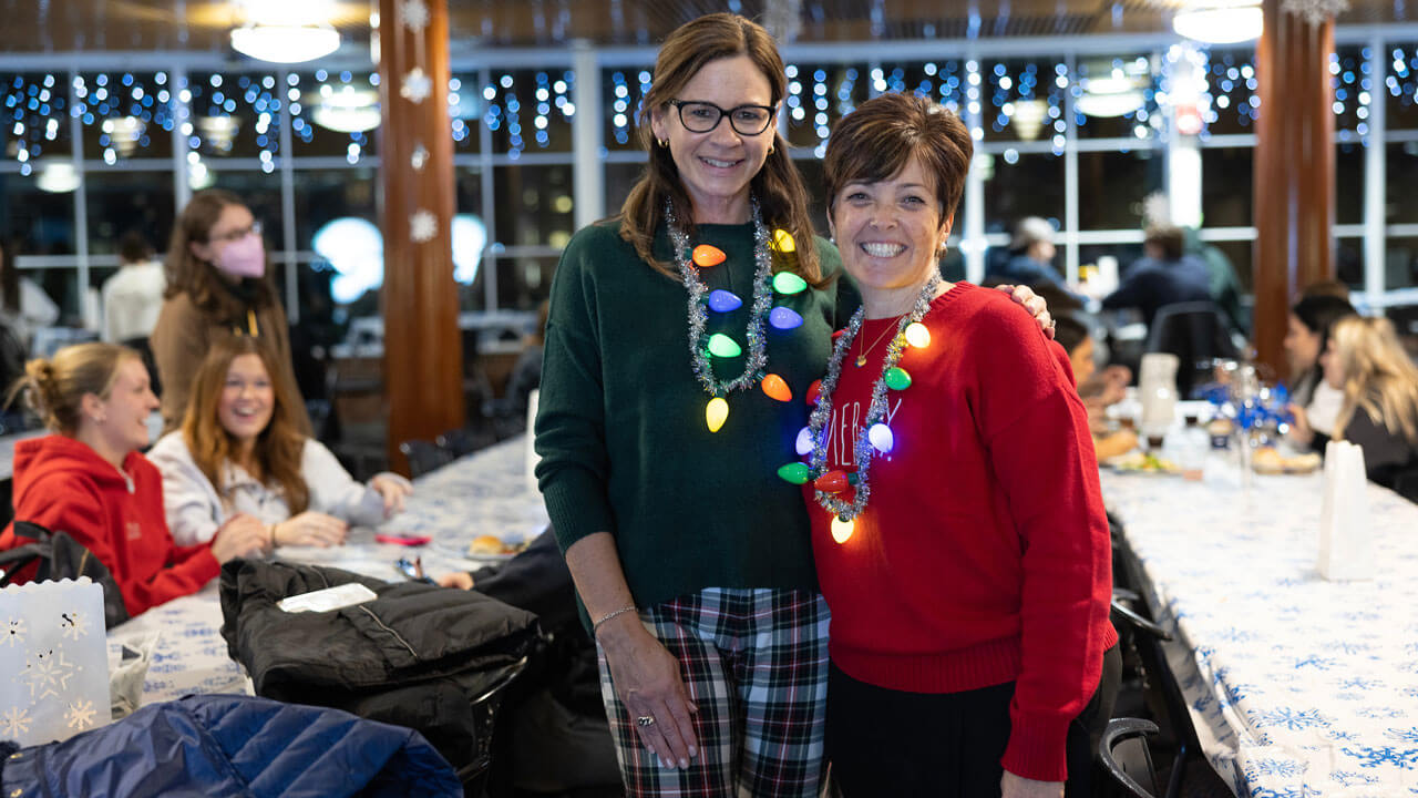 Two faculty members wear christmas light necklaces at undergraduate holiday dinner.